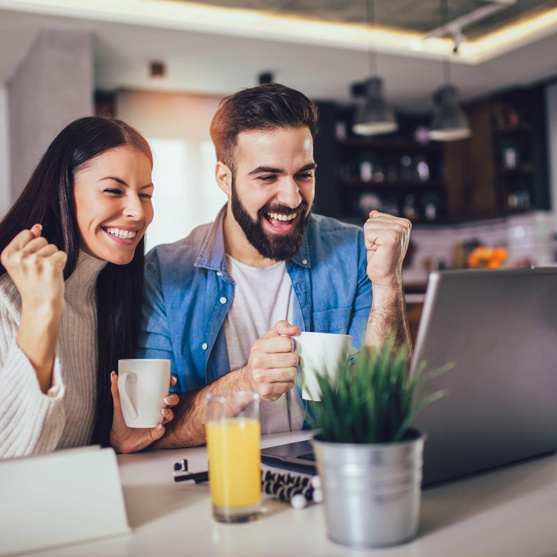 Happy couple doing business together working at home on the laptop.